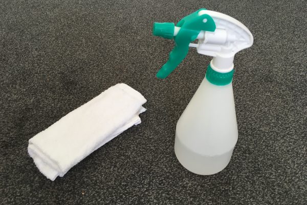 Spray bottle and white cloth to aid stain/spill removal on grey carpet