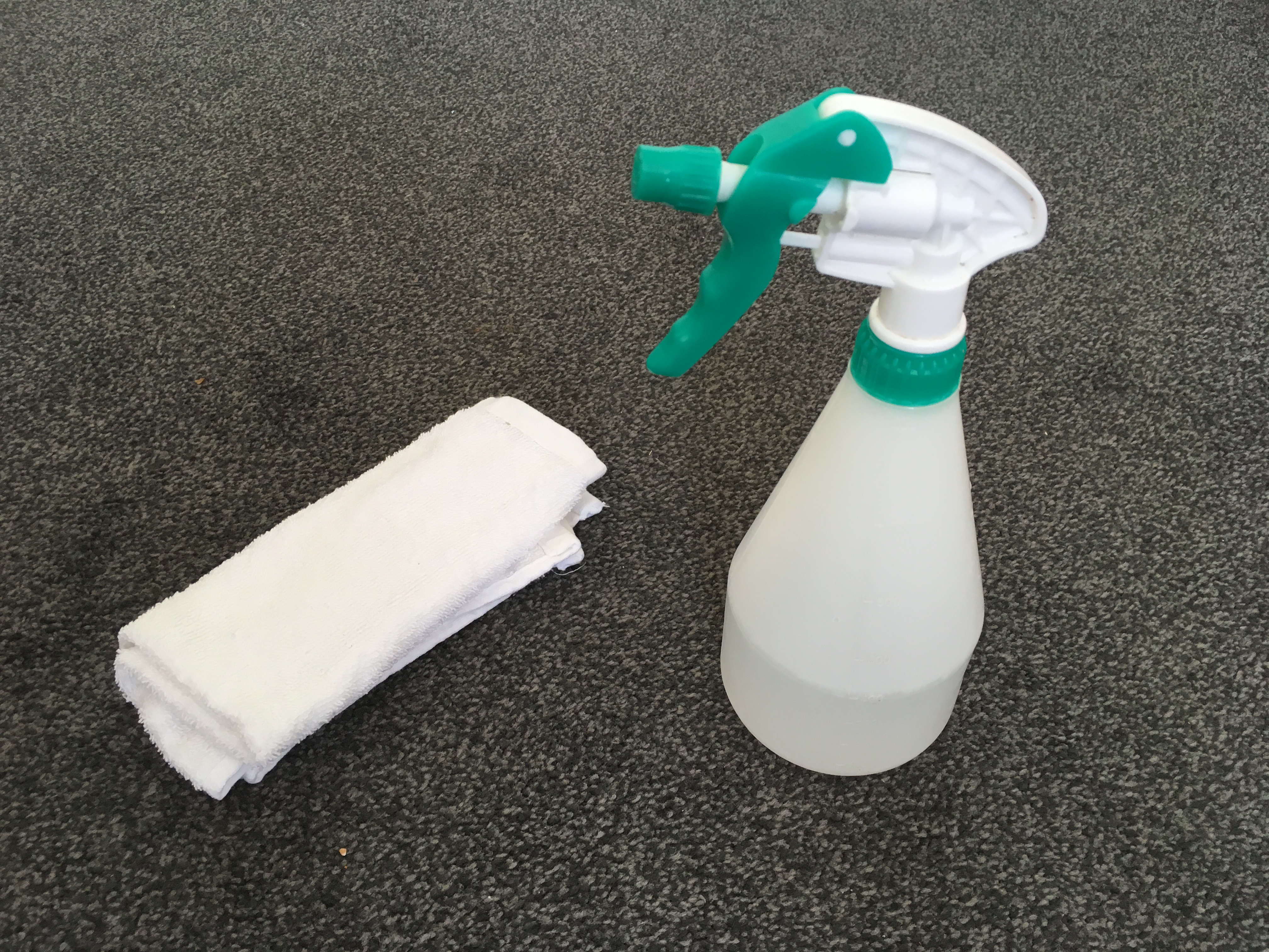 Spray bottle and white cloth to aid stain/spill removal on grey carpet
